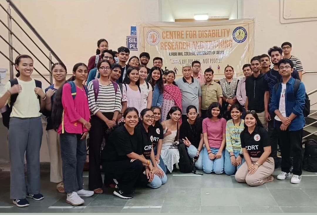 A group of around 30 students and faculty from Kirori Mal College's Centre for Disability Research and Training pose for a photo with a banner in the background.