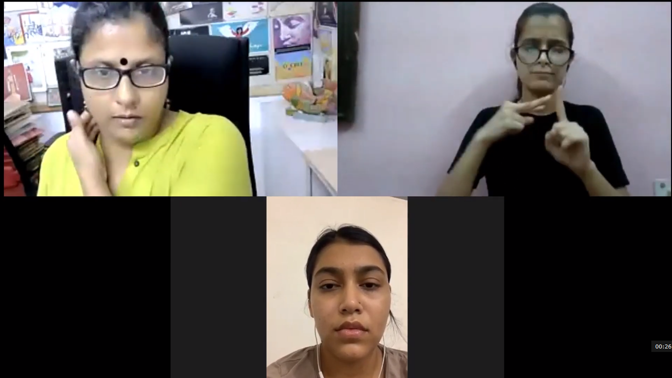A screenshot of a video call with three participants. One woman on the left is speaking, another on the top right is performing sign language, and a third woman is visible in a smaller frame at the bottom center.