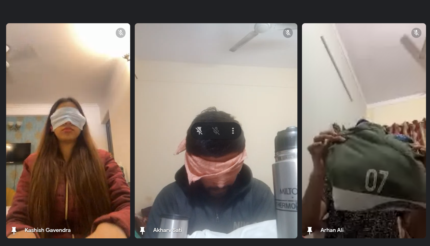 Three video call participants are shown. One woman and one man are blindfolded, while another person's face is obscured by a green jacket, likely part of a sensory or awareness exercise.