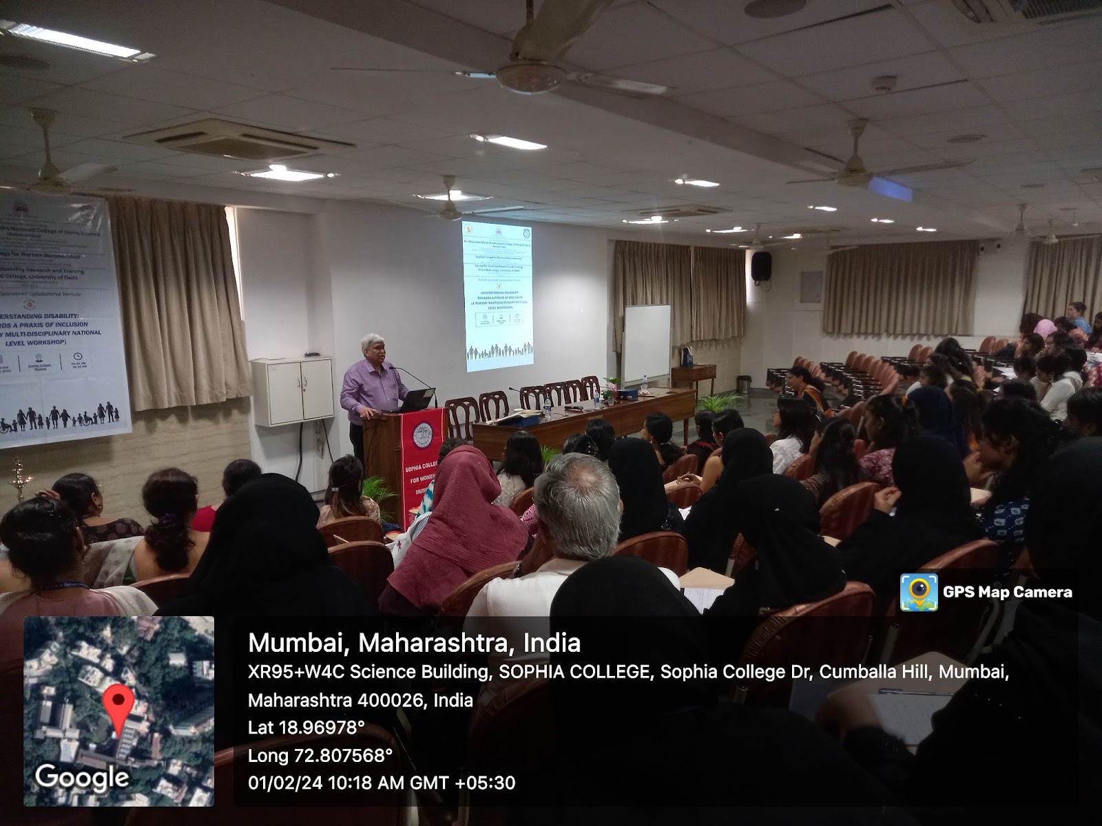 A speaker presents to a large audience in a lecture hall. A map indicates the location as Sophia College, Mumbai, India, with GPS coordinates and a timestamp of Jan 2, 2024. 