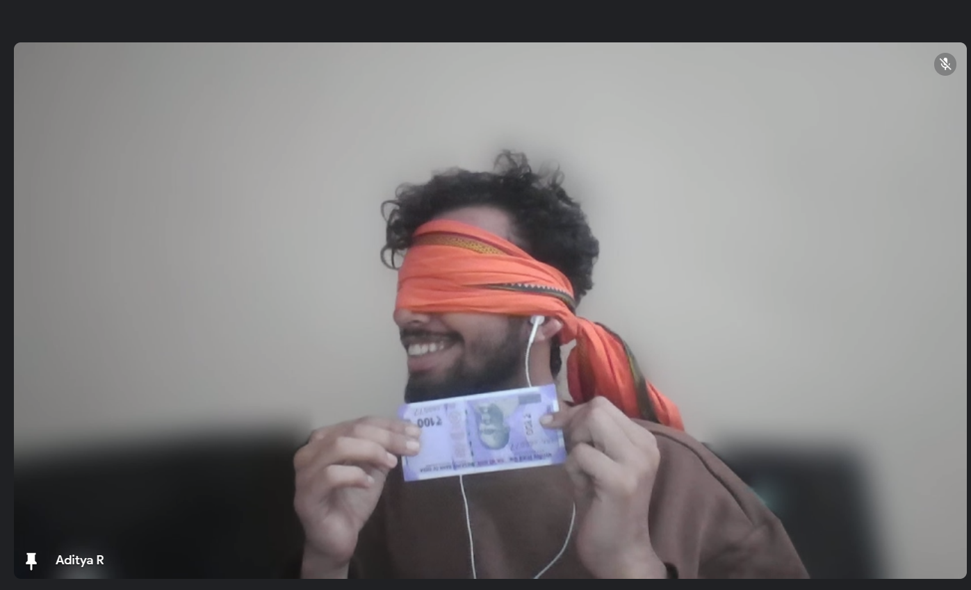 A blindfolded man on a video call smiles while holding up a 100 rupee note. This image likely captures a moment from an interactive online session focusing on sensory experiences or a fun challenge.